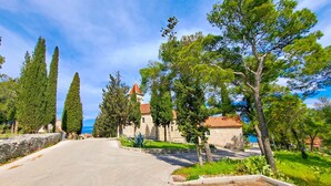 A road leading to a stone church with a red roof, surrounded by trees and greenery. - Apartments Damir - Katarina (Sutivan)