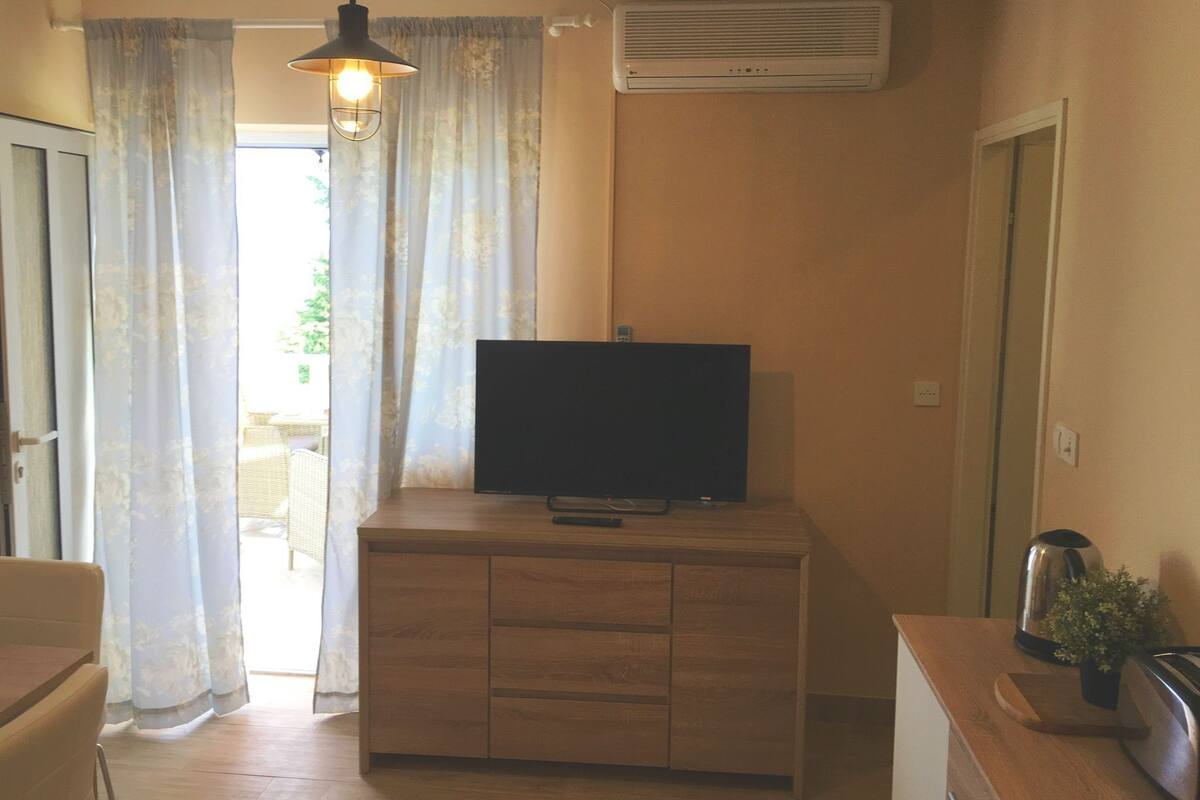 A room with a wooden cabinet, a television on top, a hanging light fixture, and an air conditioning unit on the wall.