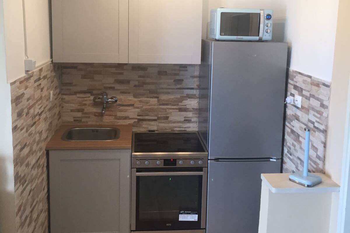 A compact kitchen with a sink, stove, oven, and a microwave on top of the refrigerator.