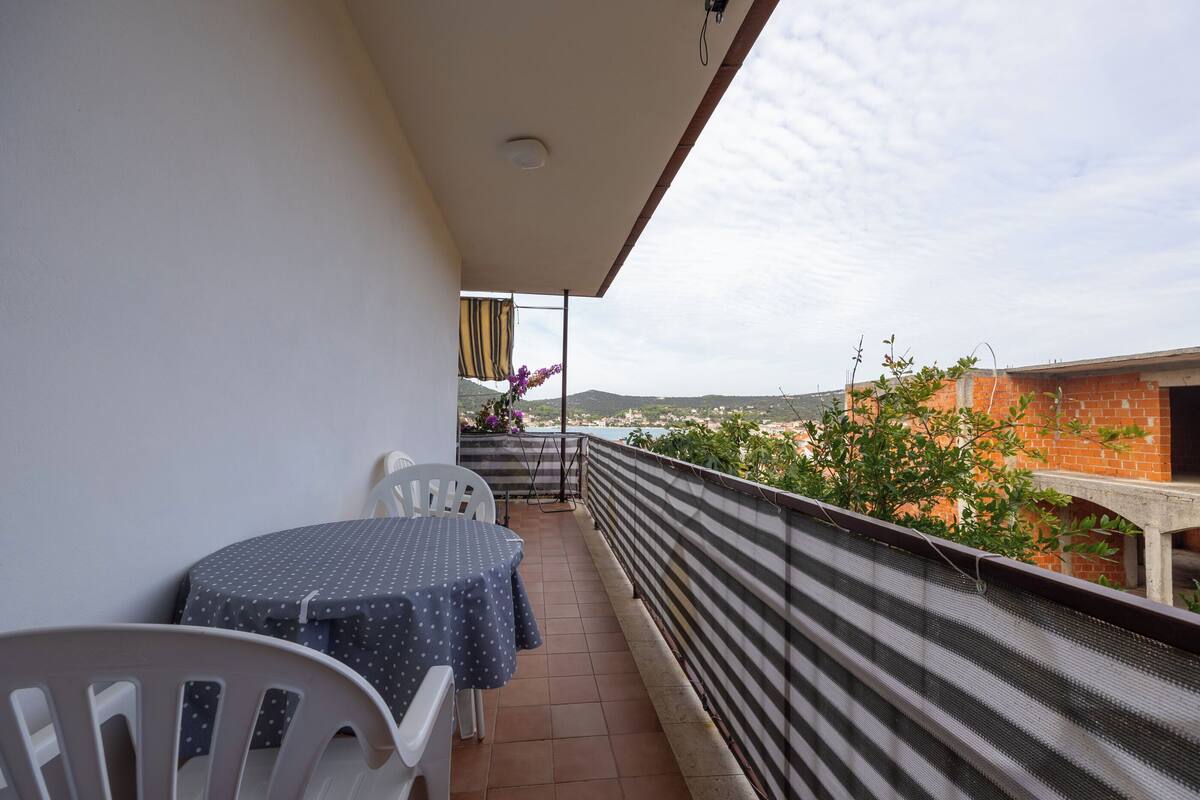 A balcony with a table and chairs, a view of a cityscape, and a striped safety barrier.