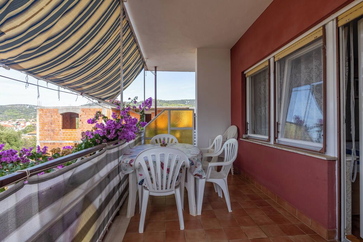 A balcony with a table and chairs, a view of the city, and purple flowers.