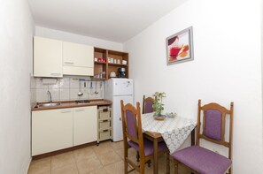 Una cocina compacta con armarios blancos, un lavamanos y una mesa de comedor con dos sillas.