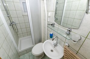 Un baño con cabina de ducha de vidrio, inodoro blanco, lavabo con espejo y toallero.