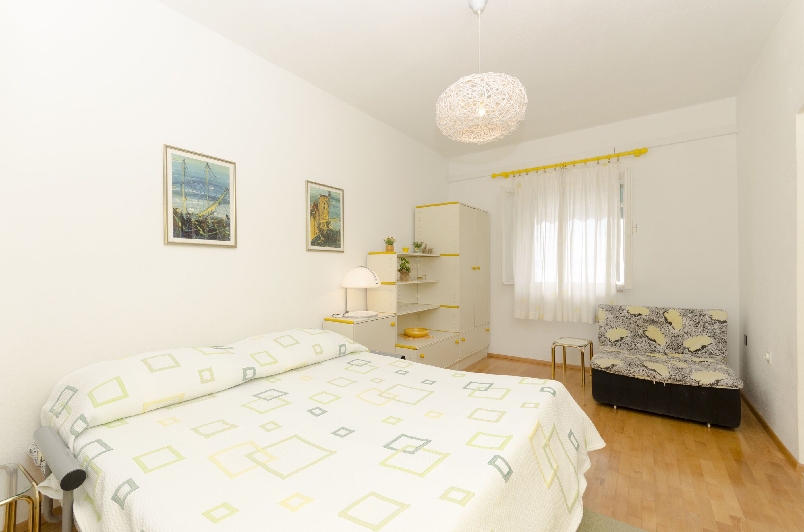 A bedroom with a bed, a nightstand, a dresser, a chair, and a hanging light fixture.