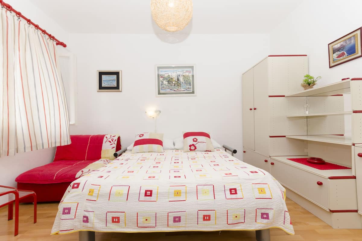 Un dormitorio con cama, una silla roja, un armario y dos cuadros en la pared.