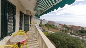Un balcon avec des chaises jaunes et une table, donnant sur une ville côtière avec ses bâtiments et offrant une vue sur la mer.