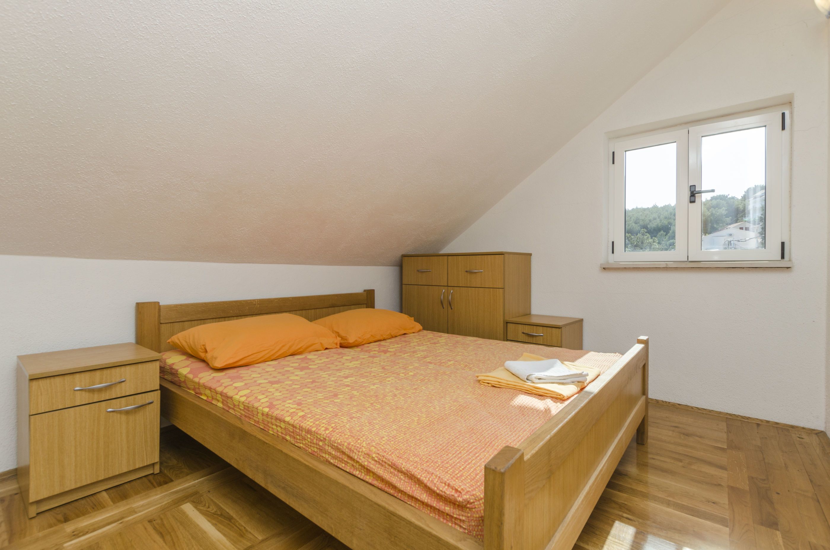 Un dormitorio con una cama de madera, una mesita de noche, un armario y una ventana con vistas a árboles.