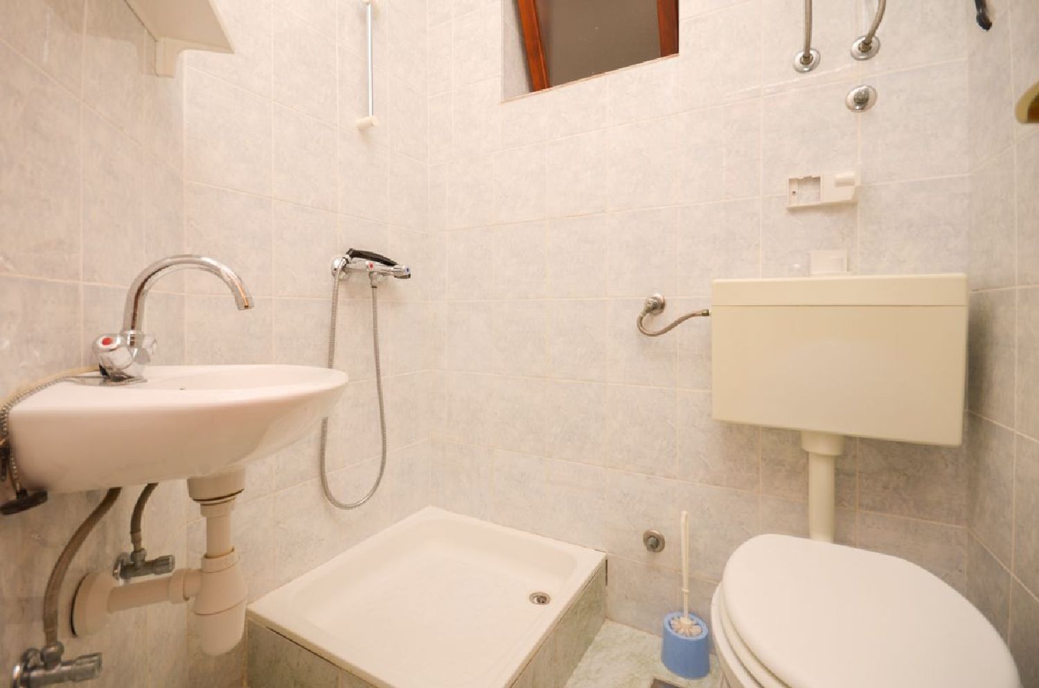 A bathroom with a sink, shower, toilet, and a small window.