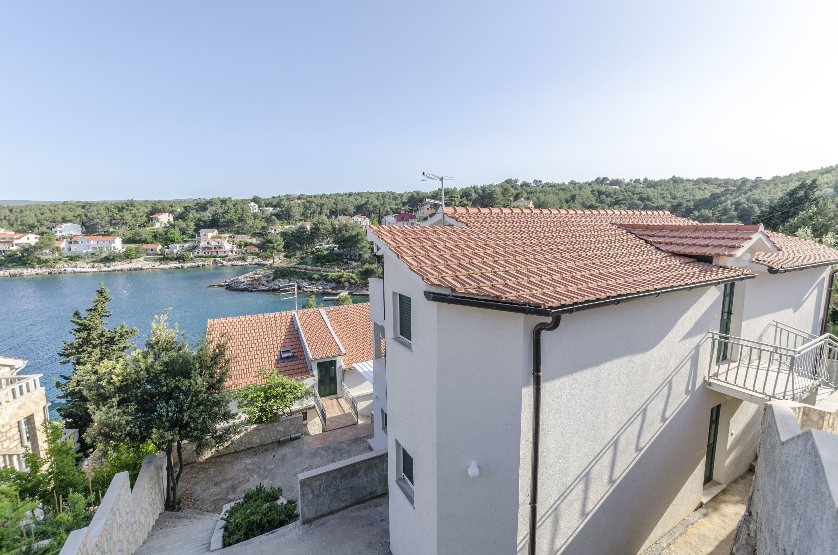 A coastal building with a tiled roof, a balcony, and a view of the sea and surrounding houses.