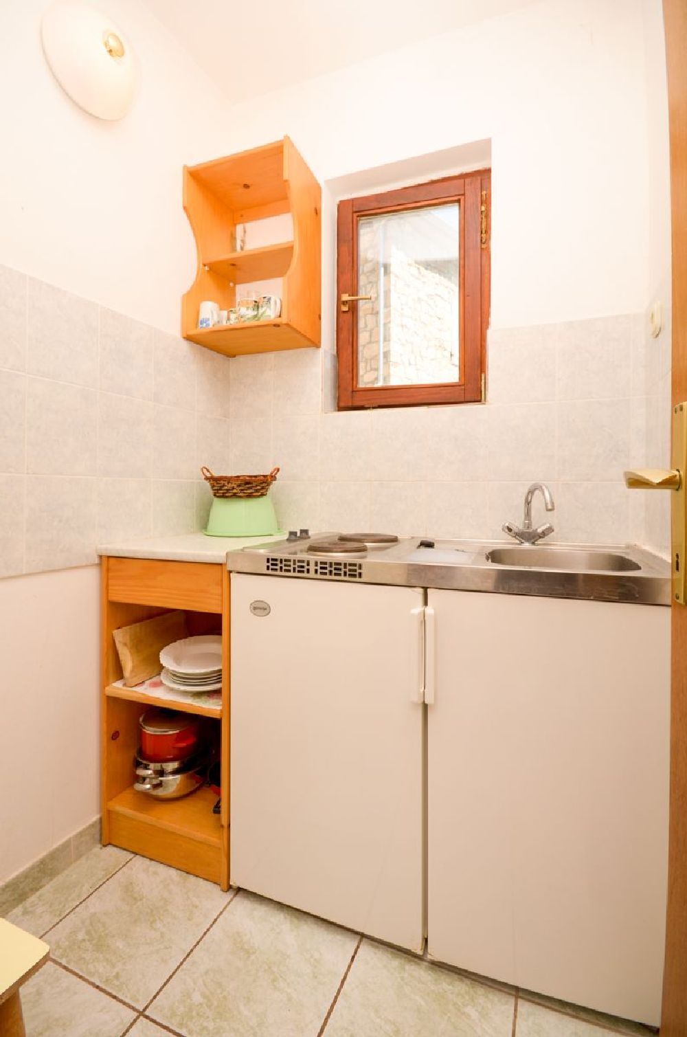 Una cocina compacta con un lavamanos integrado, una ventana sobre el lavamanos y un estante pequeño con vajilla.