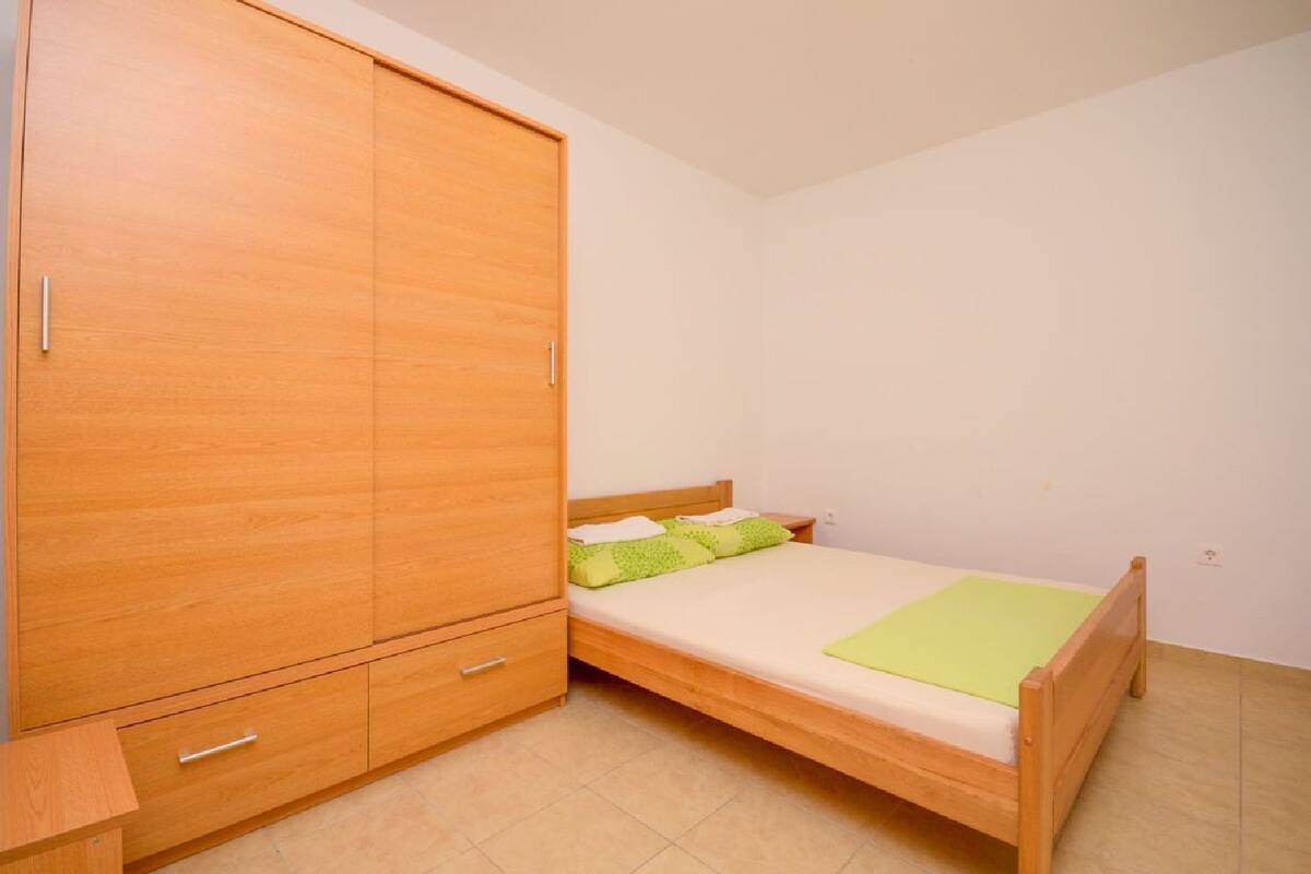 A small, single-bed room with a wooden wardrobe and a bedside table.