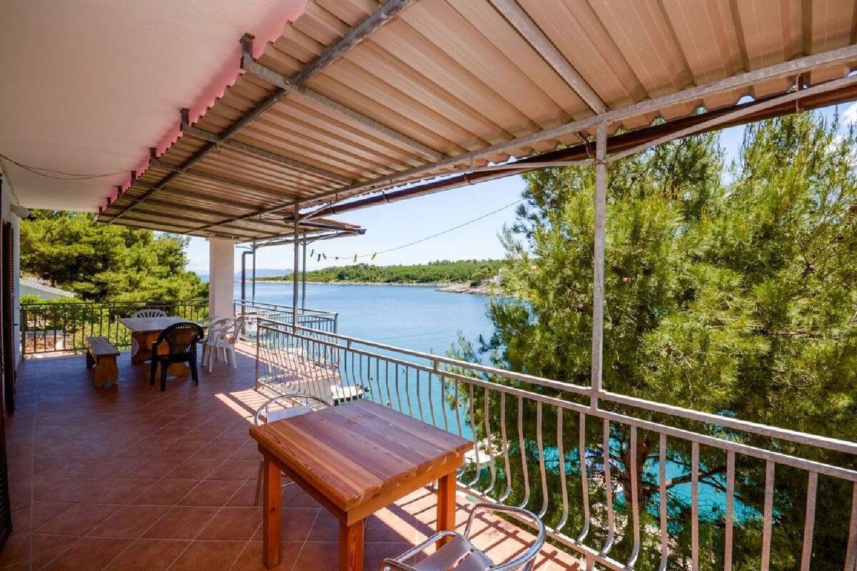 A covered outdoor area with a table and chairs, overlooking a body of water and surrounded by trees.