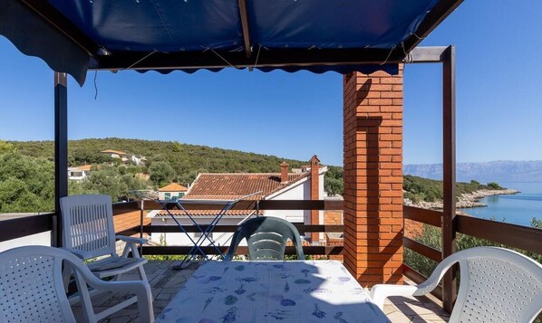 A terrace with a table and chairs, overlooking a coastal landscape with houses and a clear sky.