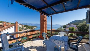 A terrace with a table and chairs, overlooking a scenic view of a body of water and distant hills. - House The Bay (Gdinj)