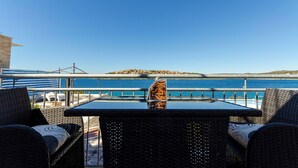 A table and chairs on a balcony overlooking a body of water with a distant island. - Apartment Mirjana (Rogoznica)