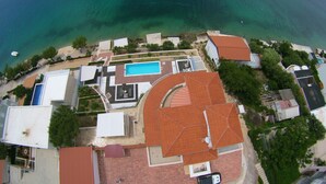 An aerial view of a coastal property with a swimming pool, multiple buildings, and a beach area. - Apartment Mirjana (Rogoznica)