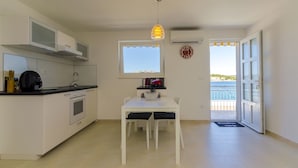 A compact kitchen with a dining area, a window with a view, and a door leading to a balcony. - Apartment Mirjana (Rogoznica)