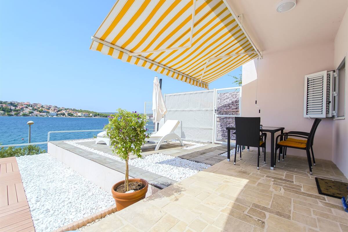 Un patio con vistas al mar, un toldo a rayas, mobiliario de exterior y una planta en maceta.