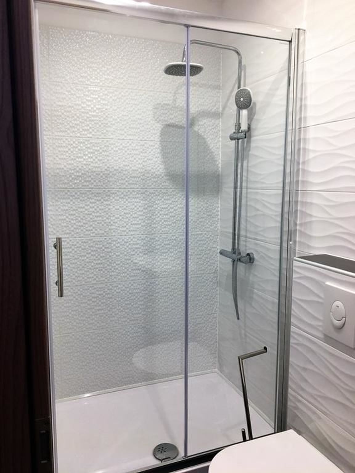 A glass-enclosed shower stall with a handheld showerhead and a wall-mounted faucet.