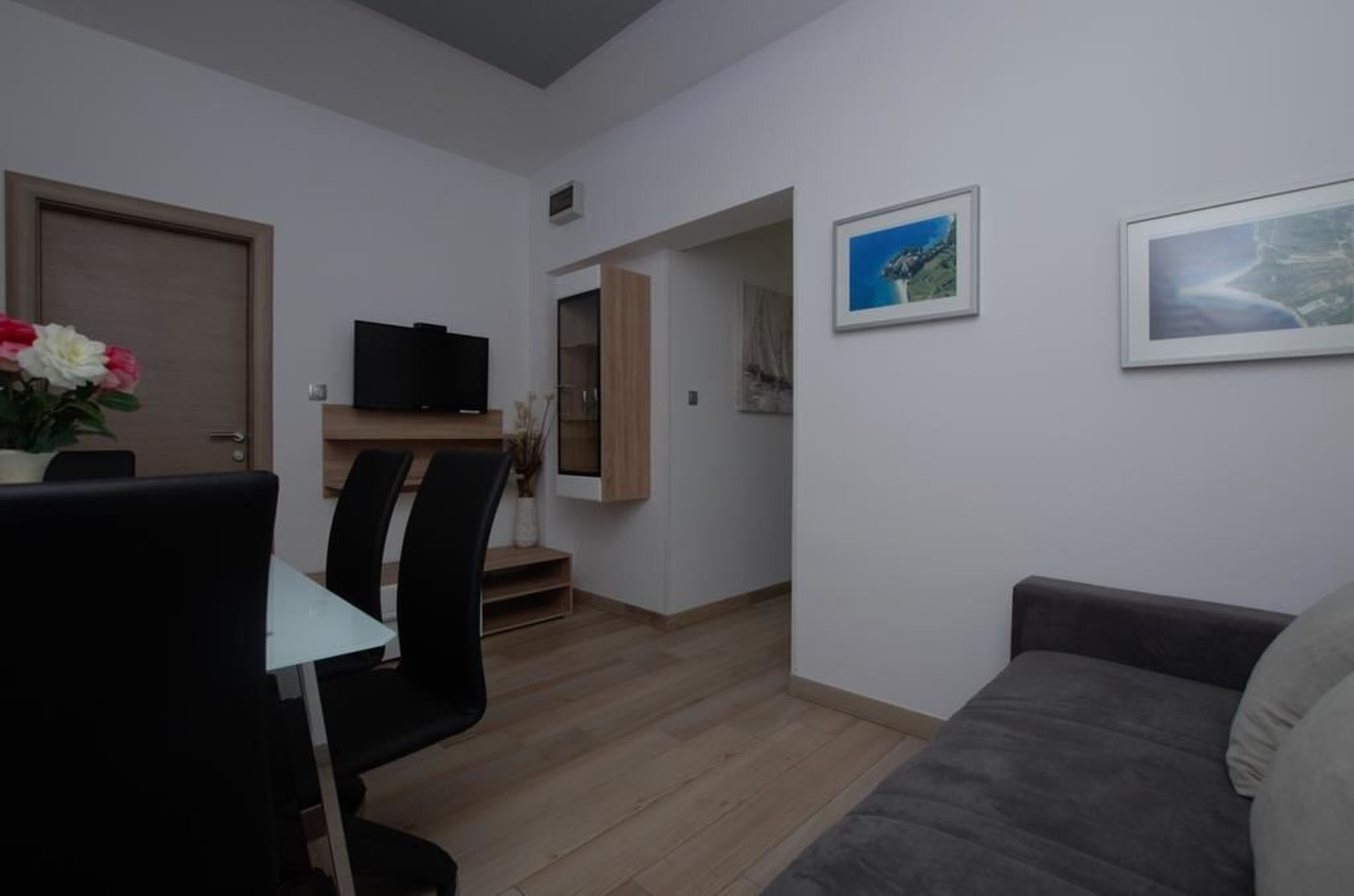 Un salon moderne avec un canapé gris, un coin repas comprenant une table et des chaises, et un téléviseur posé sur un meuble en bois.