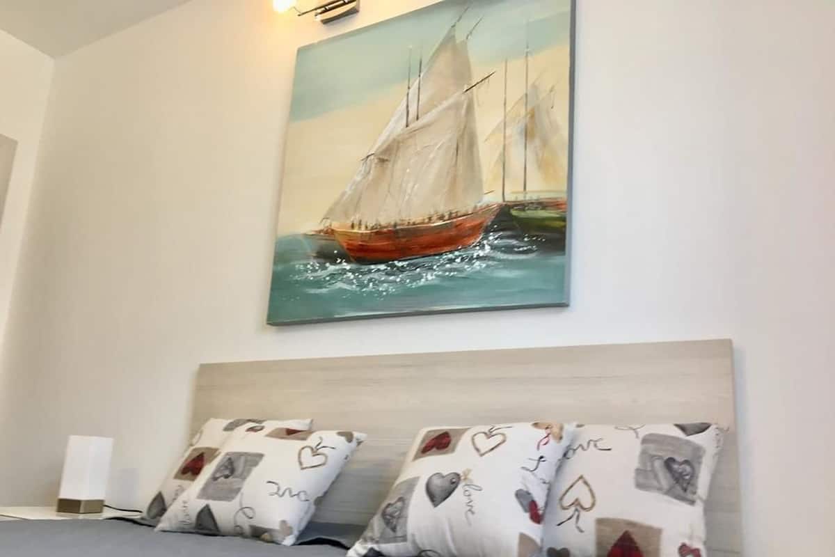 Ein Schlafzimmer mit einem Bett, zwei Kissen mit Herzmuster, einem Gemälde eines Segelboots und einer weißen Wand.