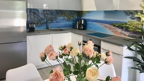 A modern kitchen with a large island, a coffee maker, and a view of a beach through the backsplash. - Apartments Fani (Bol)