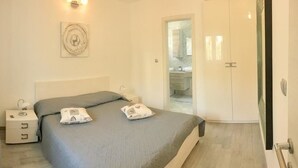 A bedroom with a bed, bedside tables, a wall-mounted artwork, and a bathroom visible through an open door. - Apartments Fani (Bol)