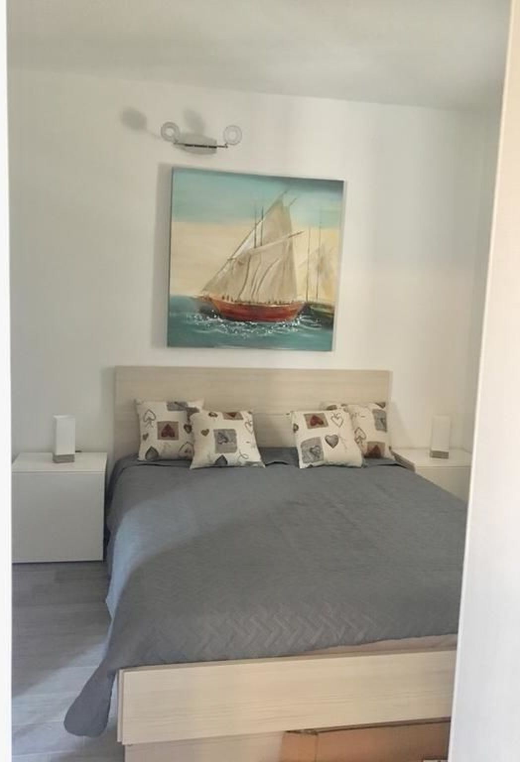 Un dormitorio con cama, dos mesitas de noche y un cuadro de un velero en la pared.
