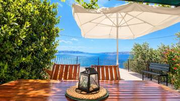 A wooden table with a lantern under a white umbrella, overlooking a scenic view of the sea and hills.