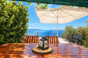 A wooden table with a lantern under a white umbrella, overlooking a scenic view of the sea and hills. - Apartment Marinera (Senj)