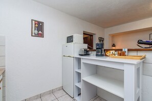 A compact kitchenette with a refrigerator, coffee maker, and a microwave on the countertop.
