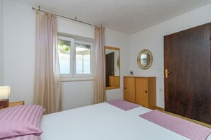 A bedroom with a bed, a wooden wardrobe, a mirror, and a window with curtains. - Apartment Marinera (Senj)