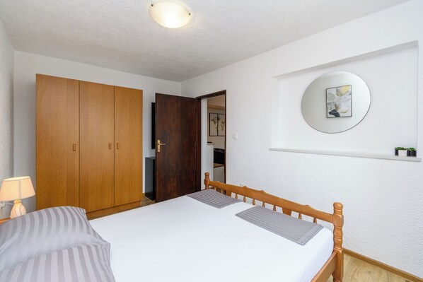 A bedroom with a bed, a wardrobe, a bedside lamp, and a wall-mounted mirror. - Apartment Marinera (Senj)