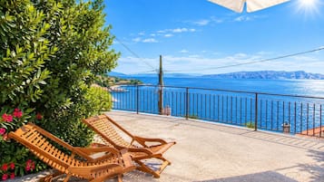 A balcony with two wooden lounge chairs, a metal railing, and a view of the sea.