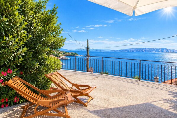 A balcony with two wooden lounge chairs, a metal railing, and a view of the sea. - Apartment Marinera (Senj)