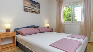 A bedroom with a bed, two bedside tables, a nightstand, a window with curtains, and a painting on the wall.