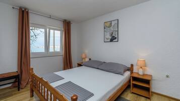 Ein Schlafzimmer mit einem Einzelbett, zwei Nachttischen, einem Fenster mit Vorhängen, einer Wandlampe und einem Gemälde.