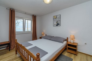 Een slaapkamer met een enkel bed, twee nachtkastjes, een raam met gordijnen, een wandlamp en een schilderij.