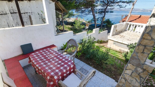 A patio with a checkered table and wicker chairs, overlooking a garden and a coastal view. - House Sliskovic (Rogac)