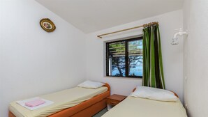 A small, single-room accommodation with two beds, a window with curtains, a bedside table, and a wall-mounted light fixture. - House Sliskovic (Rogac)