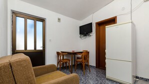 A compact room with a sofa, a dining table with chairs, a television mounted on the wall, and a refrigerator. - House Sliskovic (Rogac)