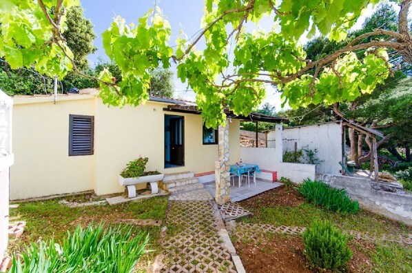 A small, single-story building with a tiled patio, a stone bench, and a table with chairs.