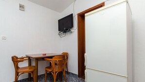 A small room with a wooden table and chairs, a white refrigerator, and a mounted television on the wall. - House Sliskovic (Rogac)