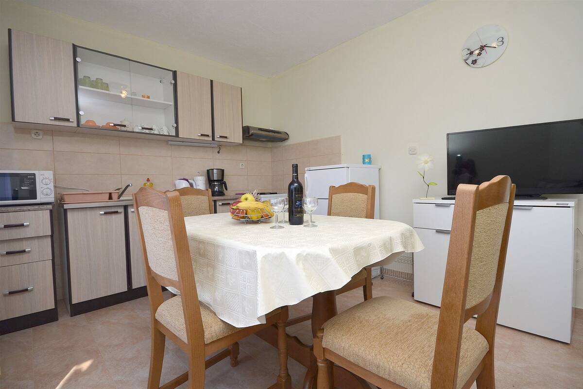 Una cucina funzionale con tavolo, sedie, frigorifero, televisione e orologio a parete.