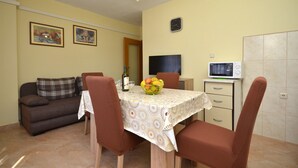 A dining area with a table set for two, a sofa, a television, and a microwave. - Apartments Katarina (Vodice)
