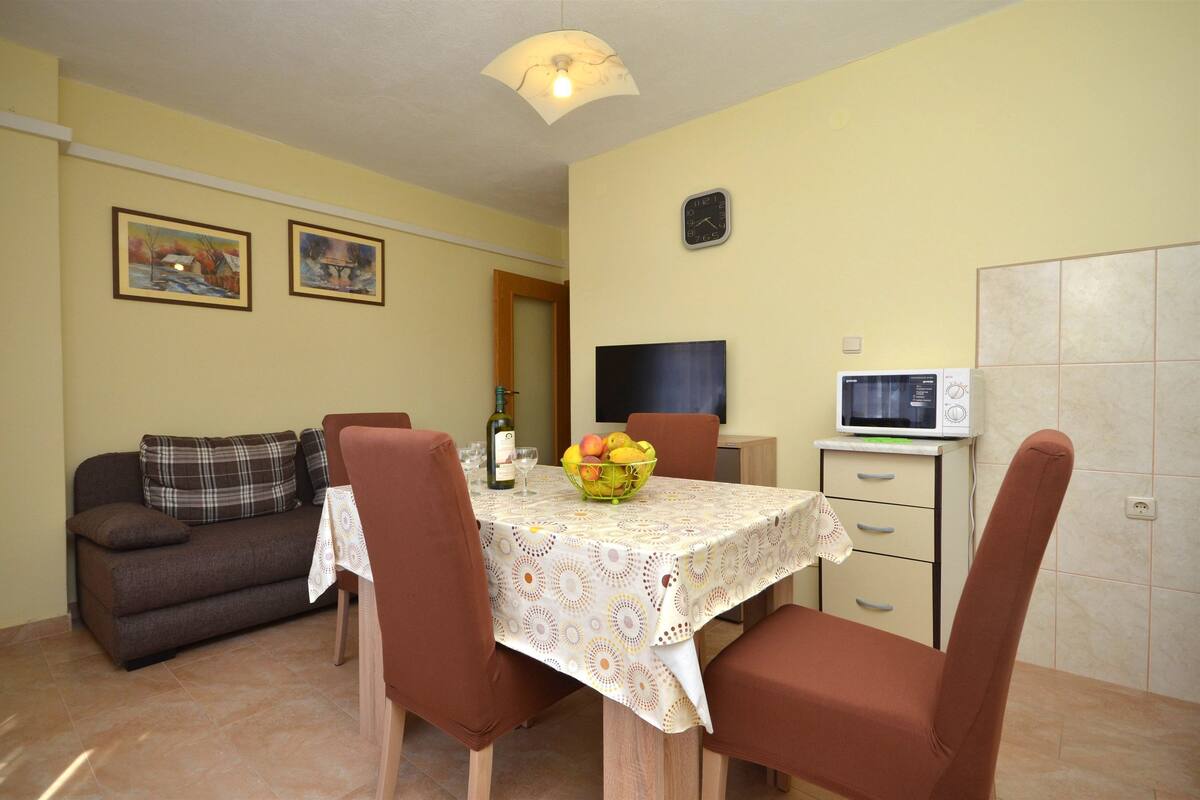 Zona pranzo con tavolo per due, divano, televisore e forno a microonde.