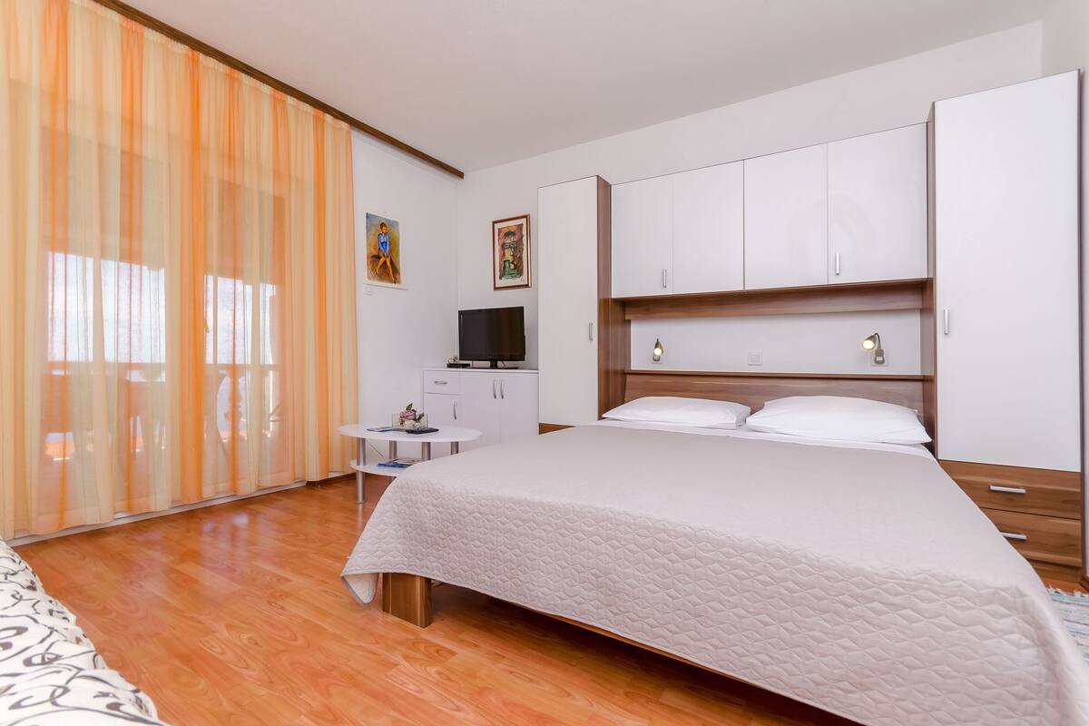 A bedroom with a bed, a TV, a small table, and a wardrobe.
