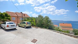En belagt indkørsel fører til et hus med tegltag, parkerede biler og havudsigt.