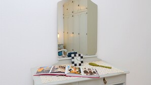 Et hvidt toiletbord med spejl, to skuffer, en lille skammel og et billede i ramme på væggen.