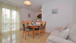 Un comedor con una mesa redonda y sillas, un sofá, y vistas al exterior a través de una ventana con cortinas translúcidas.